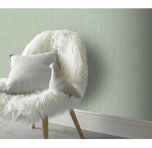 Gestructureerd vliesbehang in een wooninterieur met een fauteuil en een sierkussen voor een muur.
