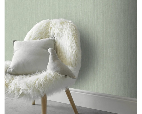 Gestructureerd vliesbehang in een wooninterieur met een fauteuil en een sierkussen voor een muur.