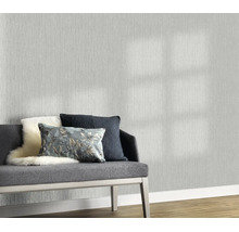 Vliesbehang met een fijne textielstructuur in een woonkamer met een gestoffeerd bankje en decoratieve kussens voor de behangen wand.