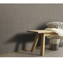 Woonruimte met vliesbehang met textielstructuur, houten bankje met kussens en vachten en gevlochten manden in een moderne inrichtingsstijl.