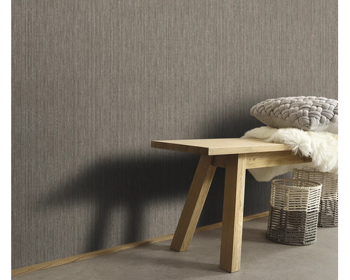 Woonruimte met vliesbehang met textielstructuur, houten bankje met kussens en vachten en gevlochten manden in een moderne inrichtingsstijl.