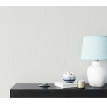 Getextureerd behang met een fijn verticaal lijnpatroon op een muur achter een zwart dressoir met een tafellamp en decoratie.
