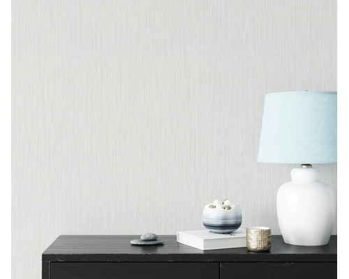 Getextureerd behang met een fijn verticaal lijnpatroon op een muur achter een zwart dressoir met een tafellamp en decoratie.