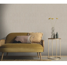 Woonkamer met effen vliesbehang met textielstructuur, een bank met kussens en een bijzettafel met glazen vaas in een modern interieur.