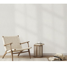 Woonruimte met behang met linnenstructuur, een fauteuil van hout en vlechtwerk, een bijzettafel en boeken op de houten vloer.