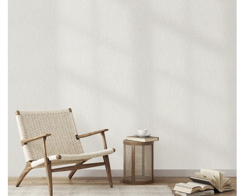 Woonruimte met behang met linnenstructuur, een fauteuil van hout en vlechtwerk, een bijzettafel en boeken op de houten vloer.