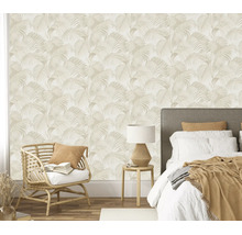 Vliesbehang met palmbladpatroon in een slaapkamer met rotan fauteuil en tweepersoonsbed.