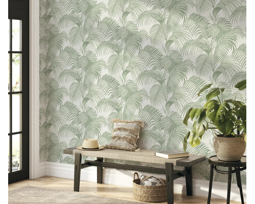 Woonruimte met vliesbehang met palmbladpatroon in tropische stijl, houten bank, sierkussens, strooien hoed en kamerplant in gevlochten mand.