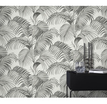 Behang met palmbladmotief, aangebracht op een muur achter een moderne zwarte bijzettafel met decoratie.