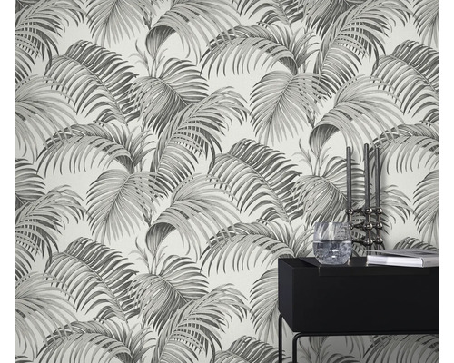 Behang met palmbladmotief, aangebracht op een muur achter een moderne zwarte bijzettafel met decoratie.