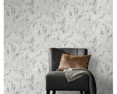 Vliesbehang met gestructureerde betonlook achter een moderne fauteuil met kussen en plaid.