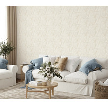 Woonkamer met licht vliesbehang met subtiel bladpatroon achter een witte bank en een ronde houten tafel met bloemenvaas.