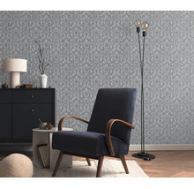 Behang met een klassiek ornamentpatroon in een stijlvol ingerichte woonkamer met een gestoffeerde fauteuil en een ladekast.