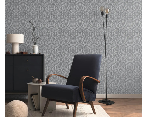 Behang met een klassiek ornamentpatroon in een stijlvol ingerichte woonkamer met een gestoffeerde fauteuil en een ladekast.