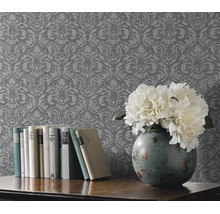 Gestructureerd vliesbehang met barok ornamentpatroon bij een houten tafel met boeken en een bloemenvaas.