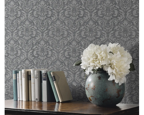 Gestructureerd vliesbehang met barok ornamentpatroon bij een houten tafel met boeken en een bloemenvaas.