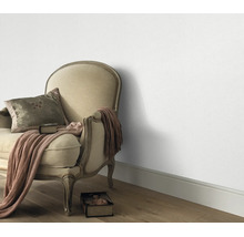 Woonruimte met klassieke gestoffeerde fauteuil en gestructureerd behang op een houten vloer.