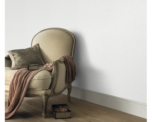 Woonruimte met klassieke gestoffeerde fauteuil en gestructureerd behang op een houten vloer.