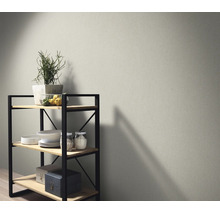 Vliesbehang met fijne textuur op een muur naast een houten rek met metalen details en decoratieve objecten in een modern interieur.