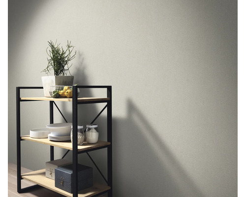 Vliesbehang met fijne textuur op een muur naast een houten rek met metalen details en decoratieve objecten in een modern interieur.