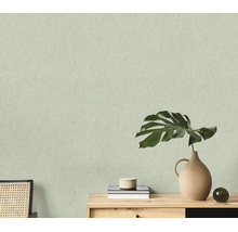 Getextureerd behang met fijne structuur op een muur achter een houten console met een monstera blad en decoratie