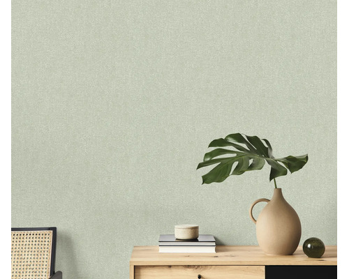 Getextureerd behang met fijne structuur op een muur achter een houten console met een monstera blad en decoratie