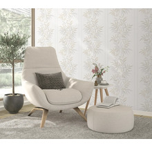 Woonkamer met modern vliesbehang met bladpatroon op de achtergrond, comfortabele fauteuil met voetenbank en plant in een licht interieur.