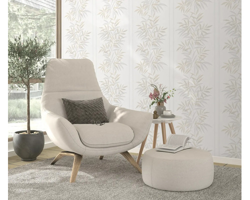 Woonkamer met modern vliesbehang met bladpatroon op de achtergrond, comfortabele fauteuil met voetenbank en plant in een licht interieur.