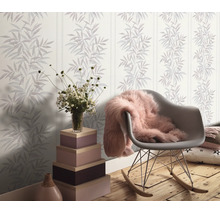 Woonkamer met vliesbehang met bamboepatroon en strepen, een schommelstoel en een decoratieve zuil van gestapelde houten kisten.