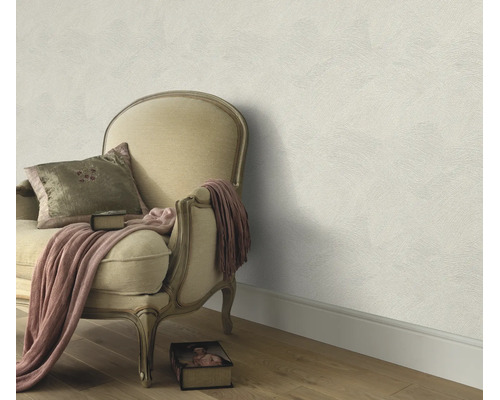 Gestructureerd vliesbehang op een muur gecombineerd met een antieke gestoffeerde fauteuil en een deken in een klassieke woonkamer.