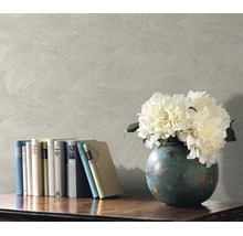 Getextureerd vliesbehang met veegstructuur als achtergrond voor een boekenplank met boeken en een vaas met bloemen.