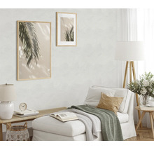 Woonkamer met licht vliesbehang met textuur, comfortabele chaise longue, houten elementen, vloerlamp en twee muurafbeeldingen met palmmotief.