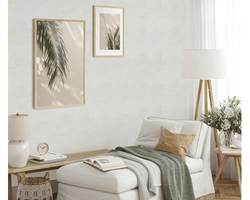 Woonkamer met licht vliesbehang met textuur, comfortabele chaise longue, houten elementen, vloerlamp en twee muurafbeeldingen met palmmotief.
