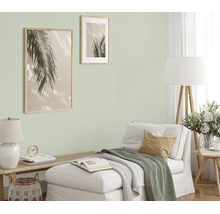 Woonkamer met lichtgroen structuurbehang, chaise longue, houten lampen en twee ingelijste palmbladafbeeldingen aan de muur voor een knusse sfeer.