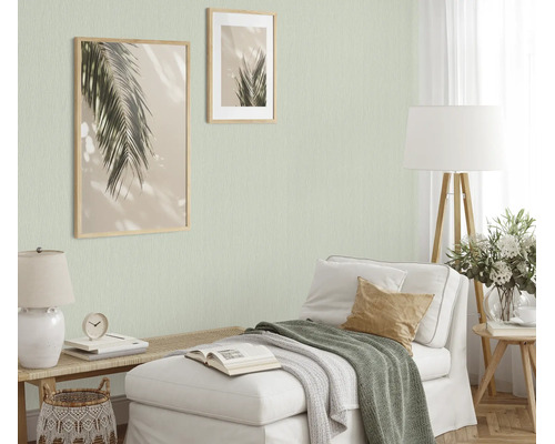 Woonkamer met lichtgroen structuurbehang, chaise longue, houten lampen en twee ingelijste palmbladafbeeldingen aan de muur voor een knusse sfeer.