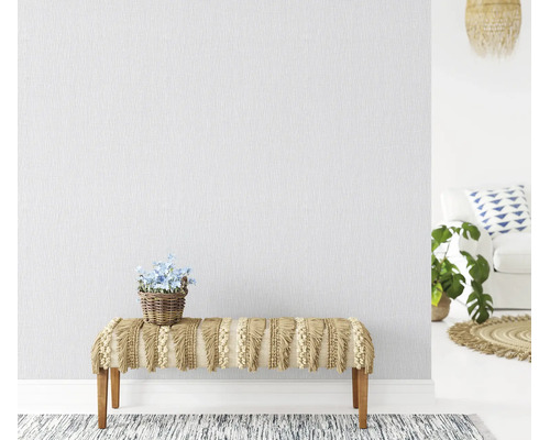 Gestructureerd vliesbehang op een muur in een lichte woonkamer met een bankje met franjes en een plant in een mand.