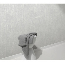 Getextureerd vliesbehang op een muur met een grijze deken op een kruk in een moderne woonruimte.