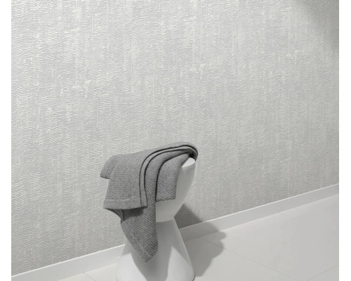 Getextureerd vliesbehang op een muur met een grijze deken op een kruk in een moderne woonruimte.