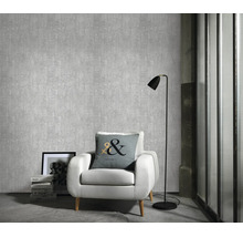 Woonkamer met gestructureerd vliesbehang, witte fauteuil, vloerlamp en sierkussen voor een muur met textuurbehang.