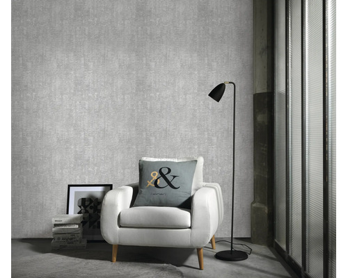 Woonkamer met gestructureerd vliesbehang, witte fauteuil, vloerlamp en sierkussen voor een muur met textuurbehang.