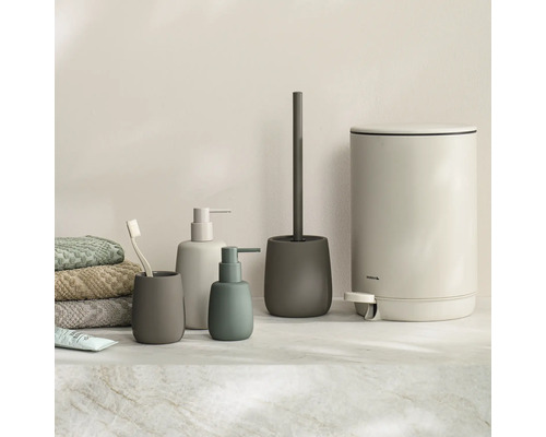 Moderne badkameraccessoireset bestaande uit zeepdispensers, tandenborstelhouder, toiletborstelhouder en pedaalemmer in mat design naast handdoeken.