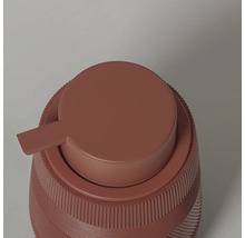 Detailopname van een terracotta zeepdispenser met een geribbelde structuur en een ronde pompkop.
