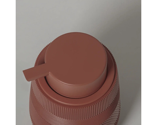 Detailopname van een terracotta zeepdispenser met een geribbelde structuur en een ronde pompkop.
