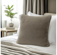Vierkant sierkussen van zacht imitatiebont in taupe, geplaatst op een bed met wit beddengoed.