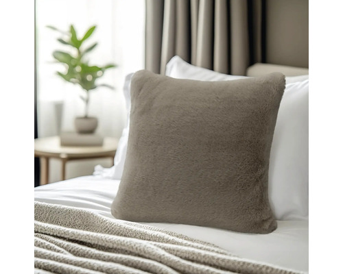 Vierkant sierkussen van zacht imitatiebont in taupe, geplaatst op een bed met wit beddengoed.