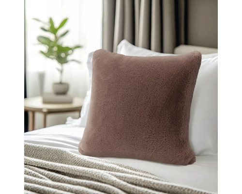 Vierkant sierkussen in imitatiebontlook op een bed met een deken en kussens op de achtergrond.