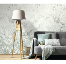 Woonkamer met vliesbehang met botanisch plantenpatroon, een grijze bank en een staande lamp met houten frame.