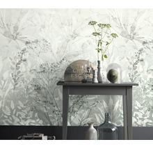 Vliesbehang met floraal bladerenmotief voor een sidetable met decoratieve glasobjecten in een lichte kamer.