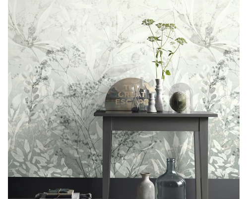 Vliesbehang met floraal bladerenmotief voor een sidetable met decoratieve glasobjecten in een lichte kamer.