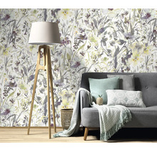 Woonkamer met vliesbehang met aquarel bloemenmotief achter een grijze bank met een statief vloerlamp op een houten vloer.